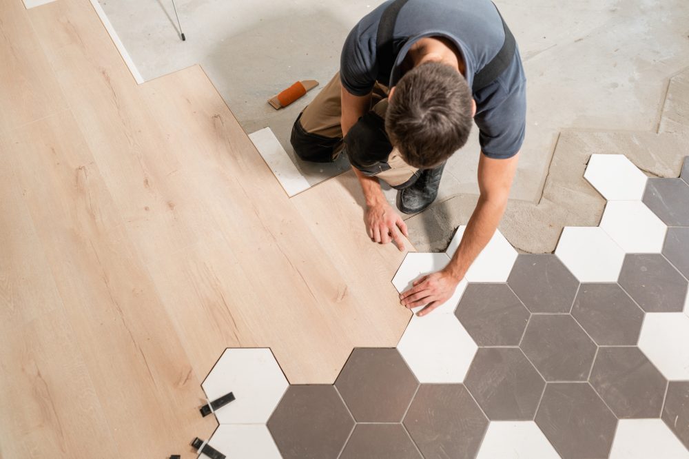 Male worker installing new wooden laminate flooring. The combination of wood panels of laminate and ceramic tiles in the form of honeycomb. Kitchen renovation.