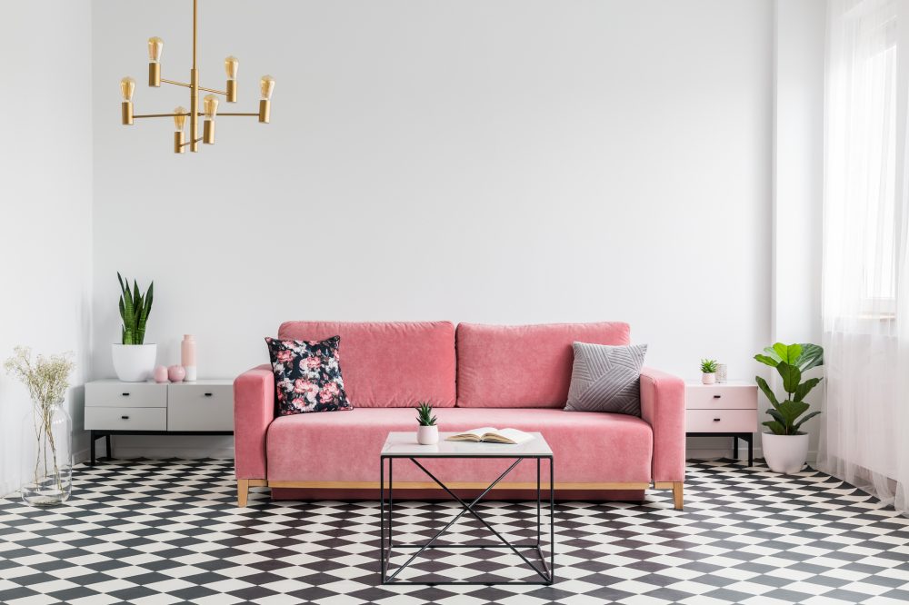 Real photo of a modern living room interior with a checkered floor, pink couch, coffee table and empty, white wall. Place your graphic here