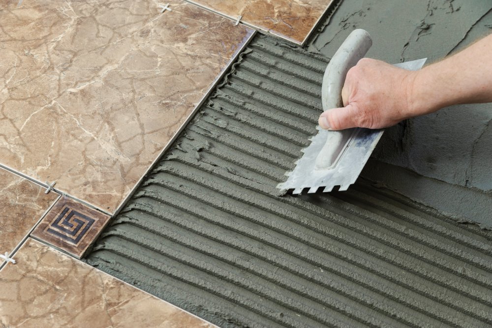 Laying Ceramic Tiles. Troweling adhesive onto a concrete floor in preparation for laying white floor tile.