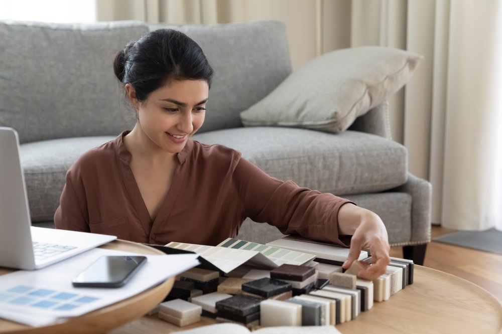 Smiling Indian woman customer choosing tile and wall paint colors from samples catalogue, young female homeowner preparing for house renovation, interior designer working on project at home